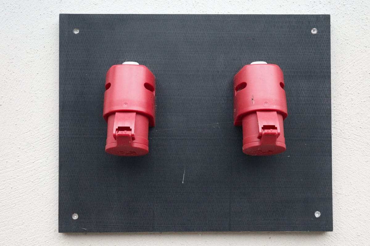 Dvi raudonos pramoninės elektros jungtys ant juodos plokštės prie sienos