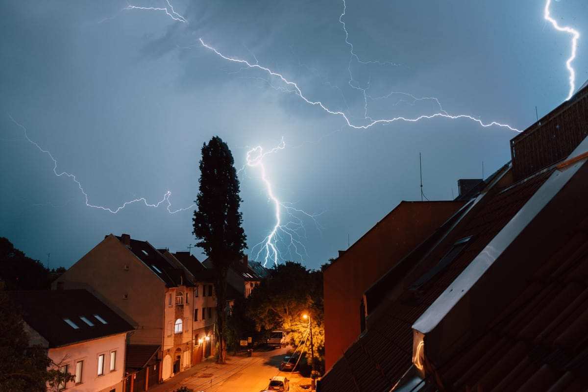 Žaibai naktiniame danguje virš gyvenamųjų namų gatvės